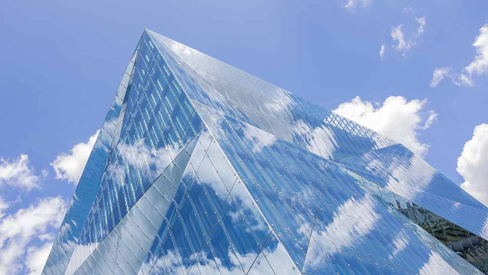 Spiegelnde Glasfassade des 3XN Cube in Berlin unter blauem Himmel