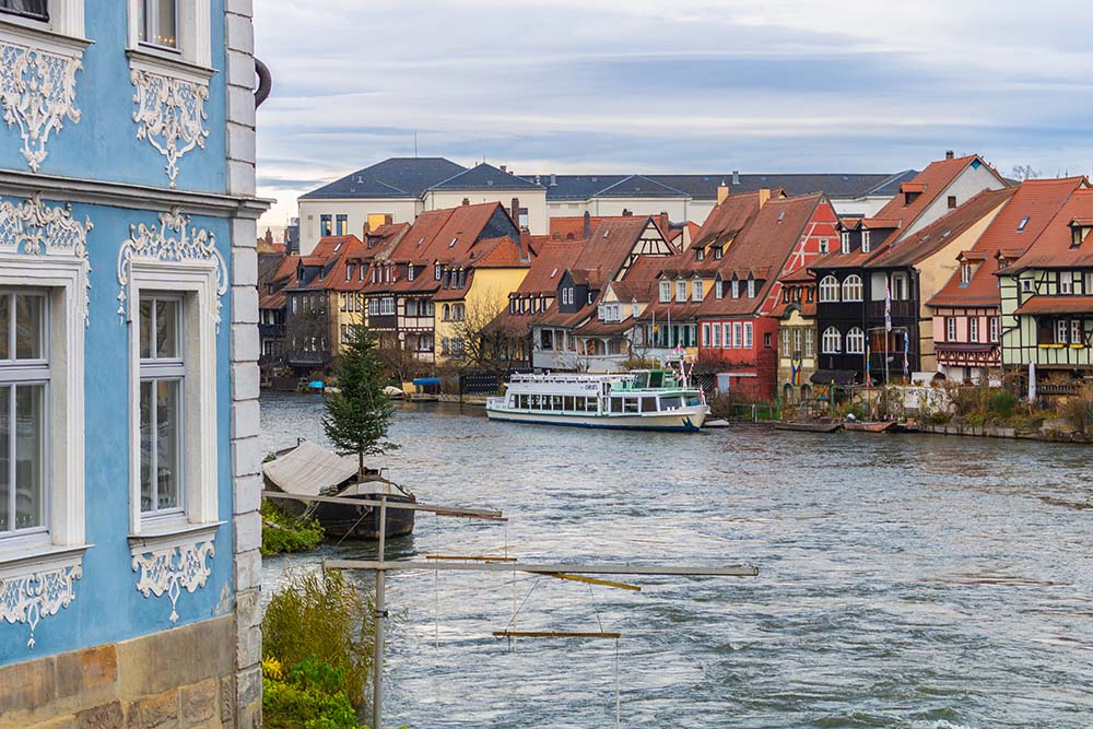 Flussufer in Bamberg mit bunten Fachwerkhäusern und Ausflugsschiff