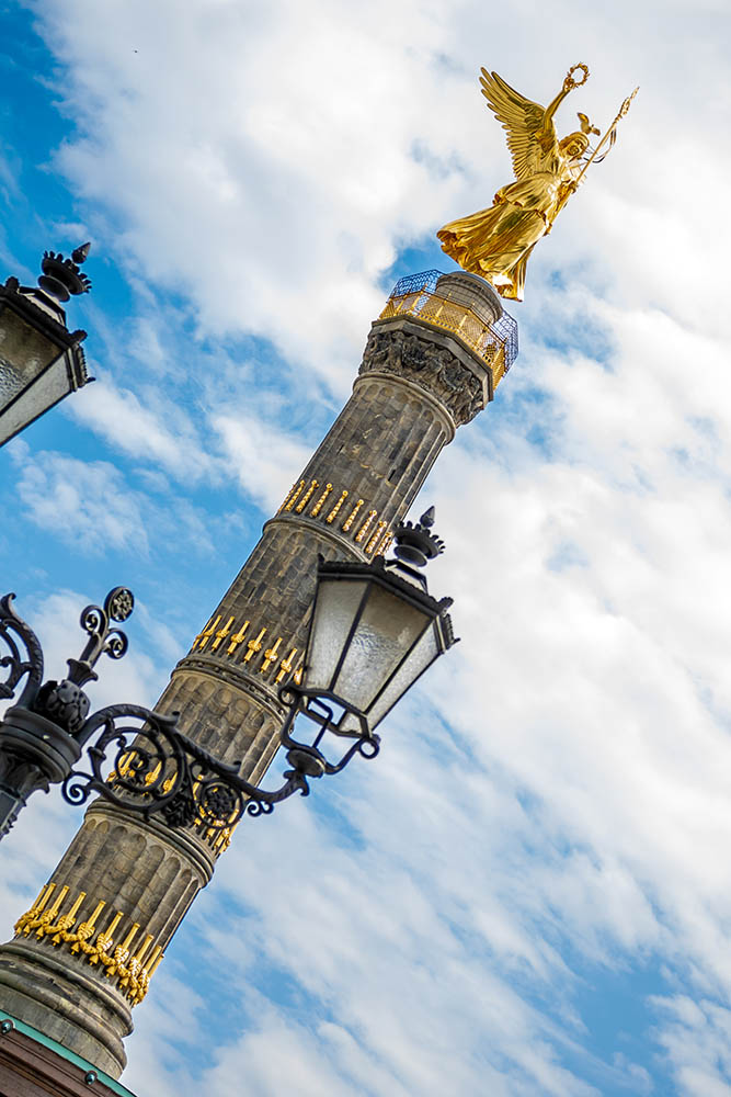 Siegessäule mit goldener Statue und historischen Laternen in Schrägansicht