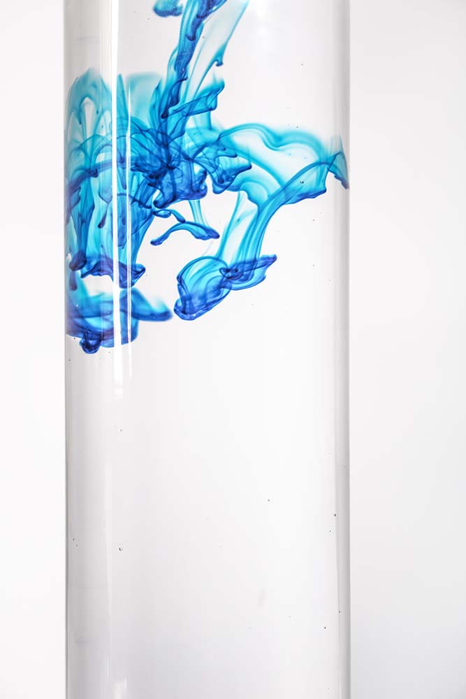 Blaue Tinte verteilt sich in klarem Wassergefäß