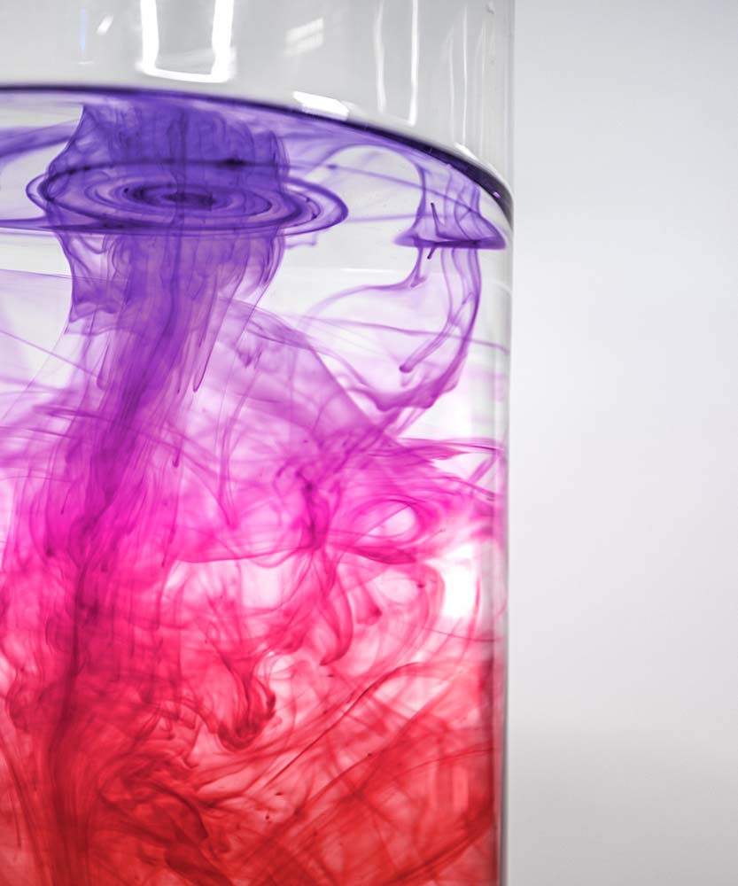 Lila und rote Tinte verteilt sich in klarem Wassergefäß