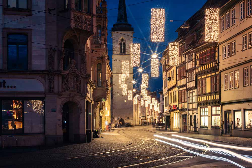 Weihnachtlich beleuchtete Marktstraße in Erfurt mit Straßenbahn‑Lichtspuren.