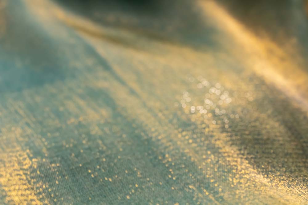 Weicher Stoff in Grün‑Gold mit schimmernden Lichtreflexen.