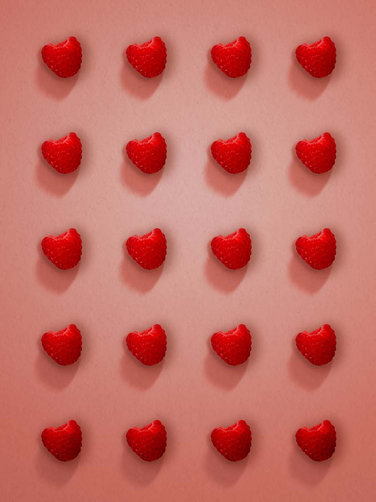 Herzförmige Himbeeren in symmetrischem Raster auf rosigem Hintergrund.