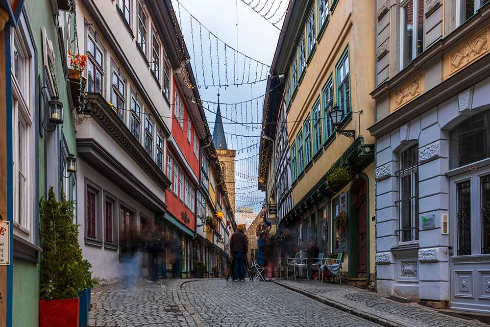 Belebte Krämerbrücke in Erfurt mit Altstadthäusern und Lichterketten.