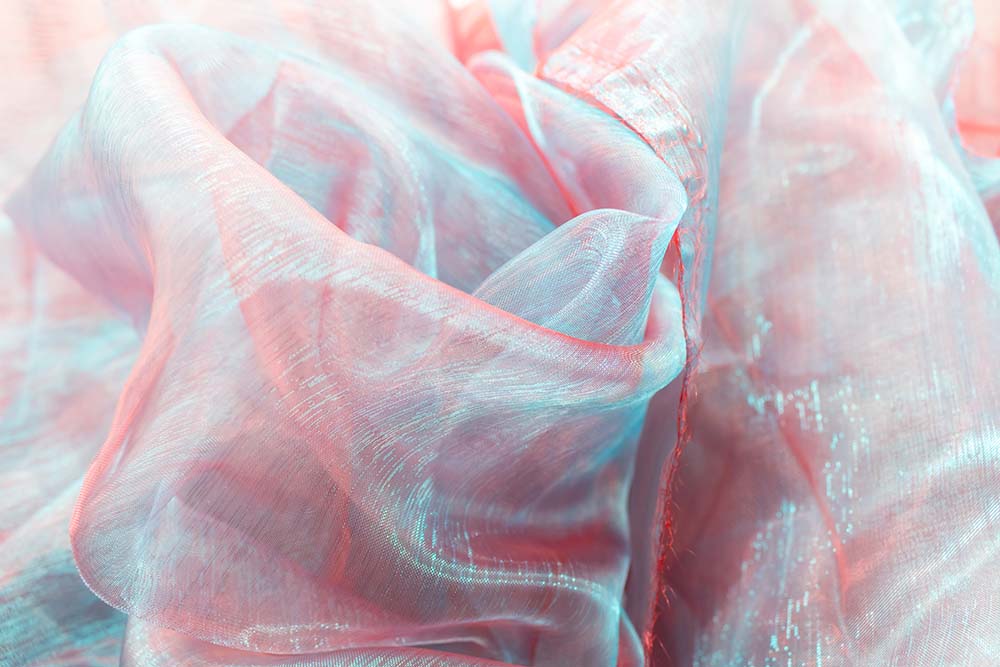 Schimmernder Organza in Blau‑Rosé mit feinen Faltenstrukturen.