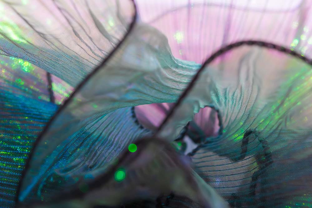 Irisierende Stofffalten in Grün, Blau und Rosé im Detail.