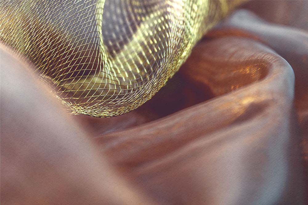 Golden schimmerndes Netz über warmen Stofffalten in weichen Linien.