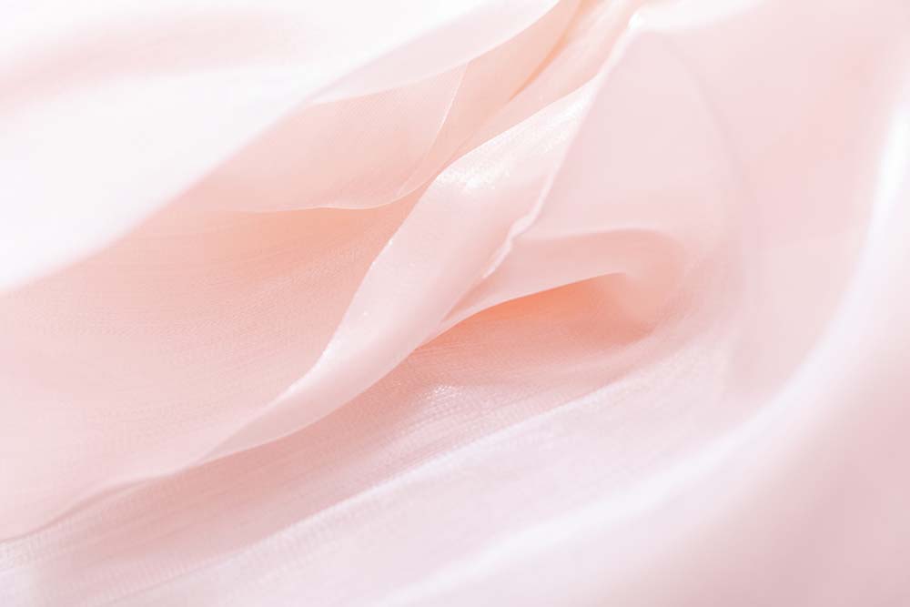 Zarte roséfarbene Stofffalten in weichem, lichtdurchlassenem Verlauf.