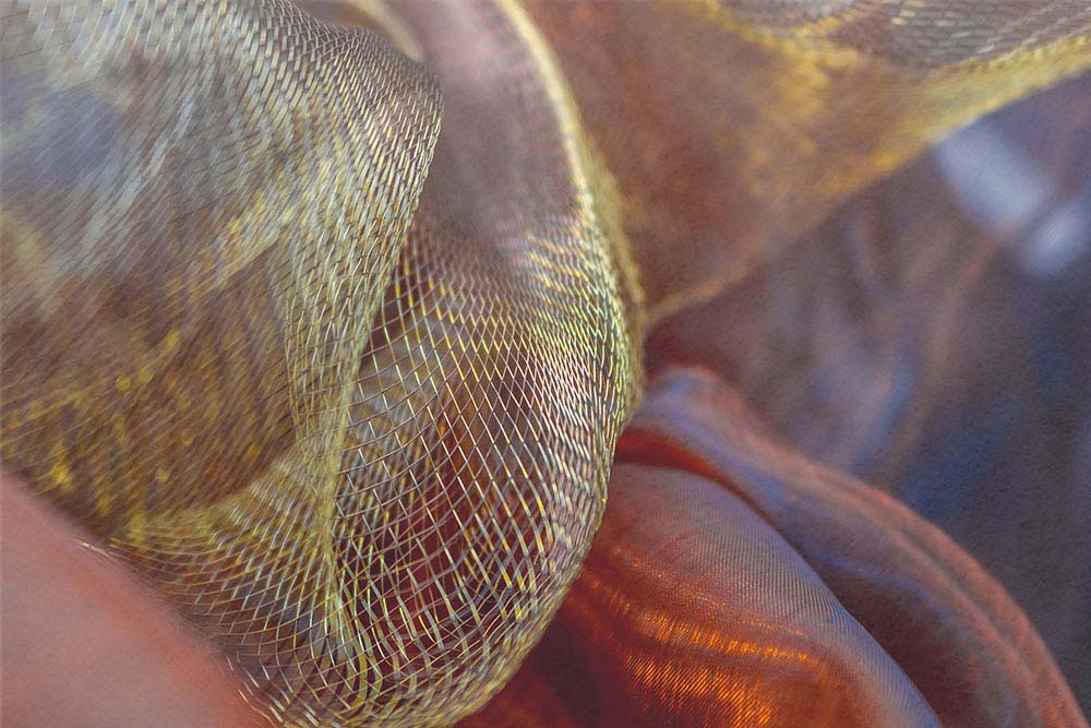 Goldenes Netz über warm getönten Stofffalten in weicher Bewegung.