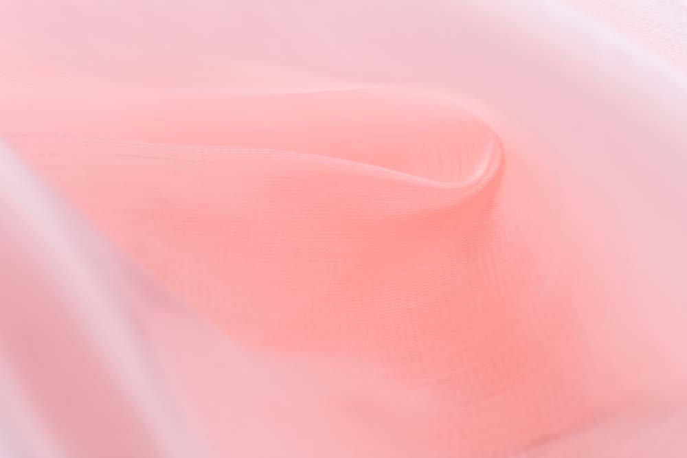 Zarte roséfarbene Stofffalte mit weichem Licht und Transparenz.