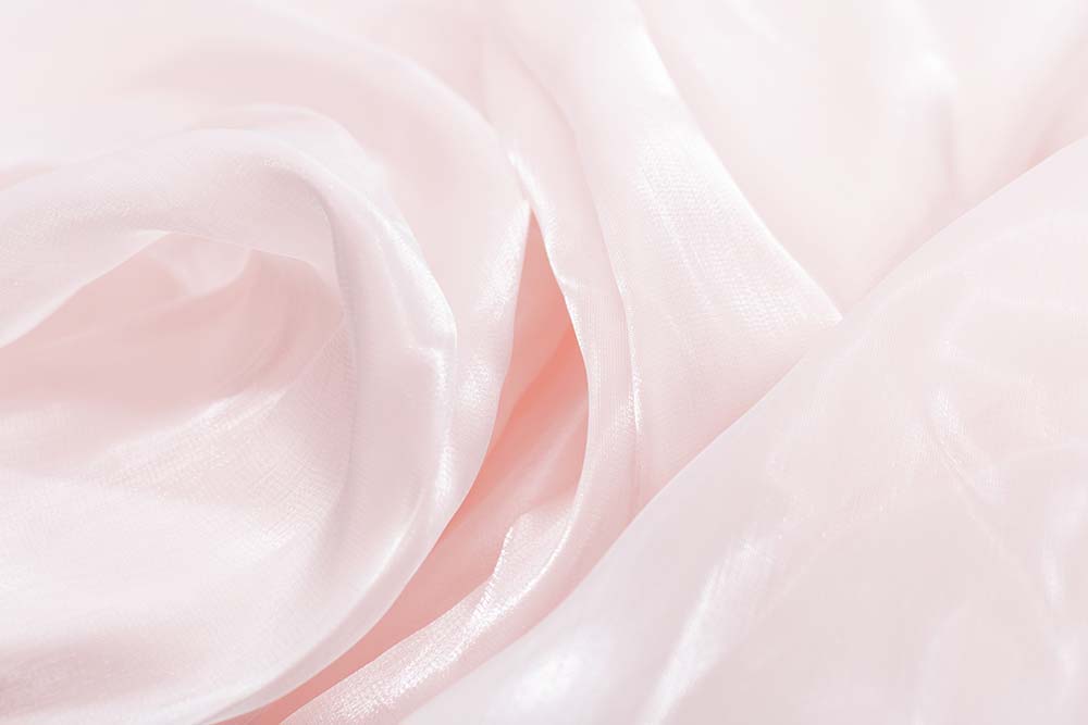 Zarte, roséfarbene Stofffalten mit weichem Glanz und feiner Struktur.
