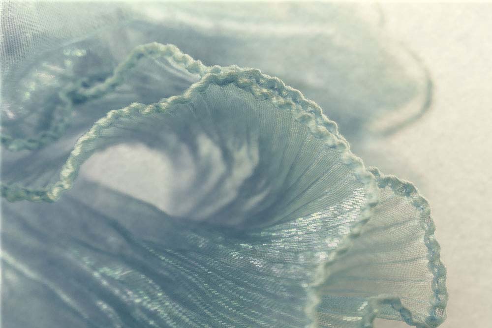 Zarte, blaugrüne Stofffaltung mit feinen, transluzenten Linien.